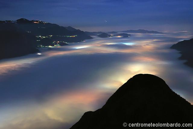 11.jpg - Ore 18.22 - La Val San Martino con, in primo piano, il Lago di Olginate (ovviamente buio). Si riconosce bene l'area di Valcava. Ai margini del lago, i paesi illuminati che sembrano trasparire con le loro luci attraverso la nebbia - AUTORE: Stefano Anghileri